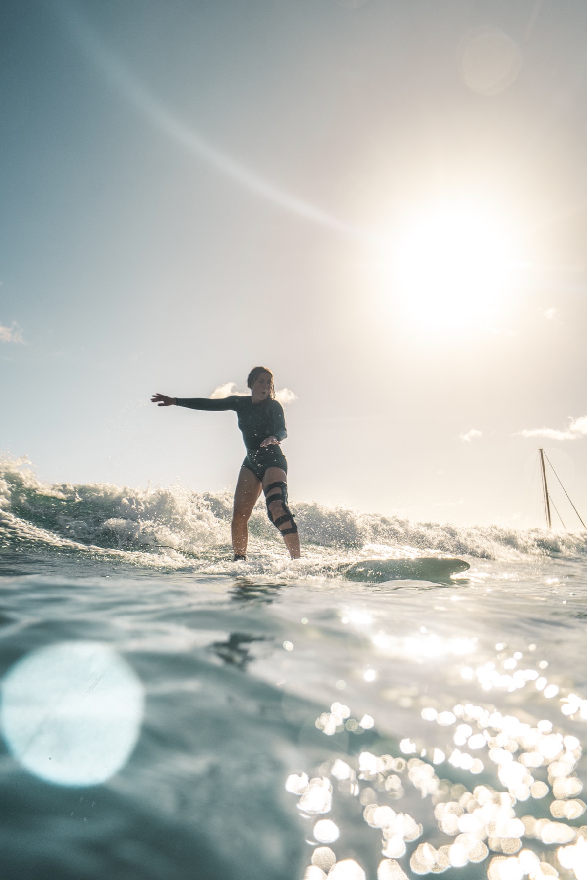 Syd Meyer riding a wave at Waikiki in her knee brace, sun behind her